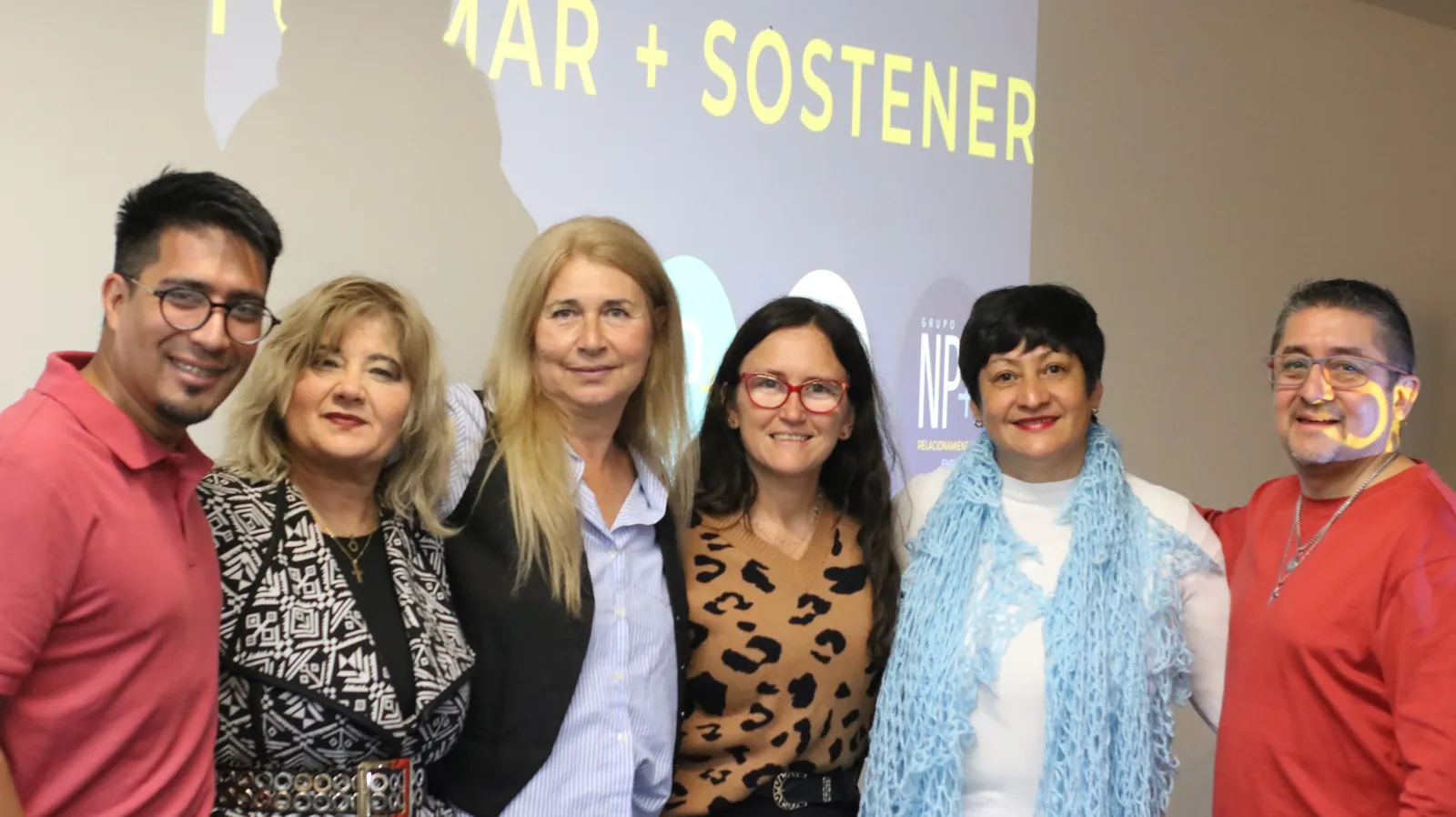 Seis integrantes de la comunidad NP+ posando frente al lema Formar + Sostener